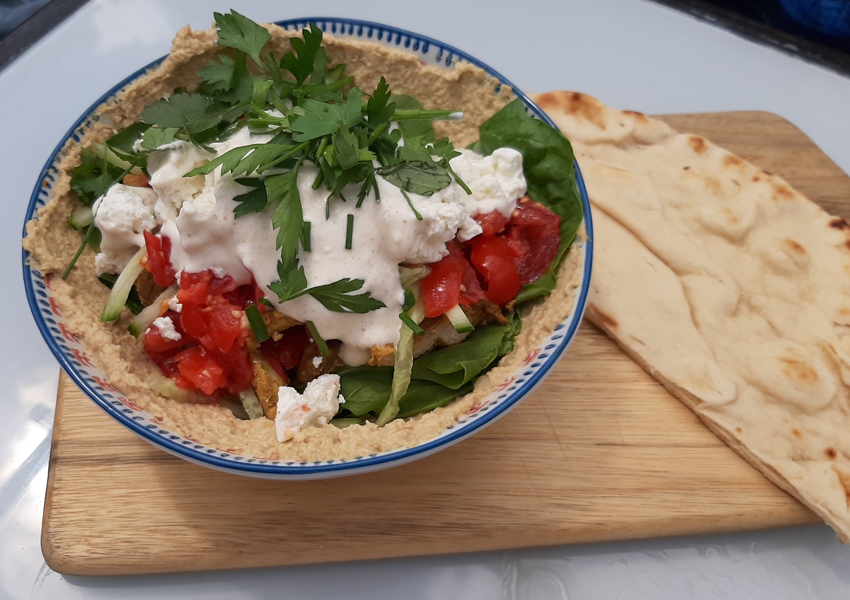 A hummus bowl topped with chicken shawarma and flatbread